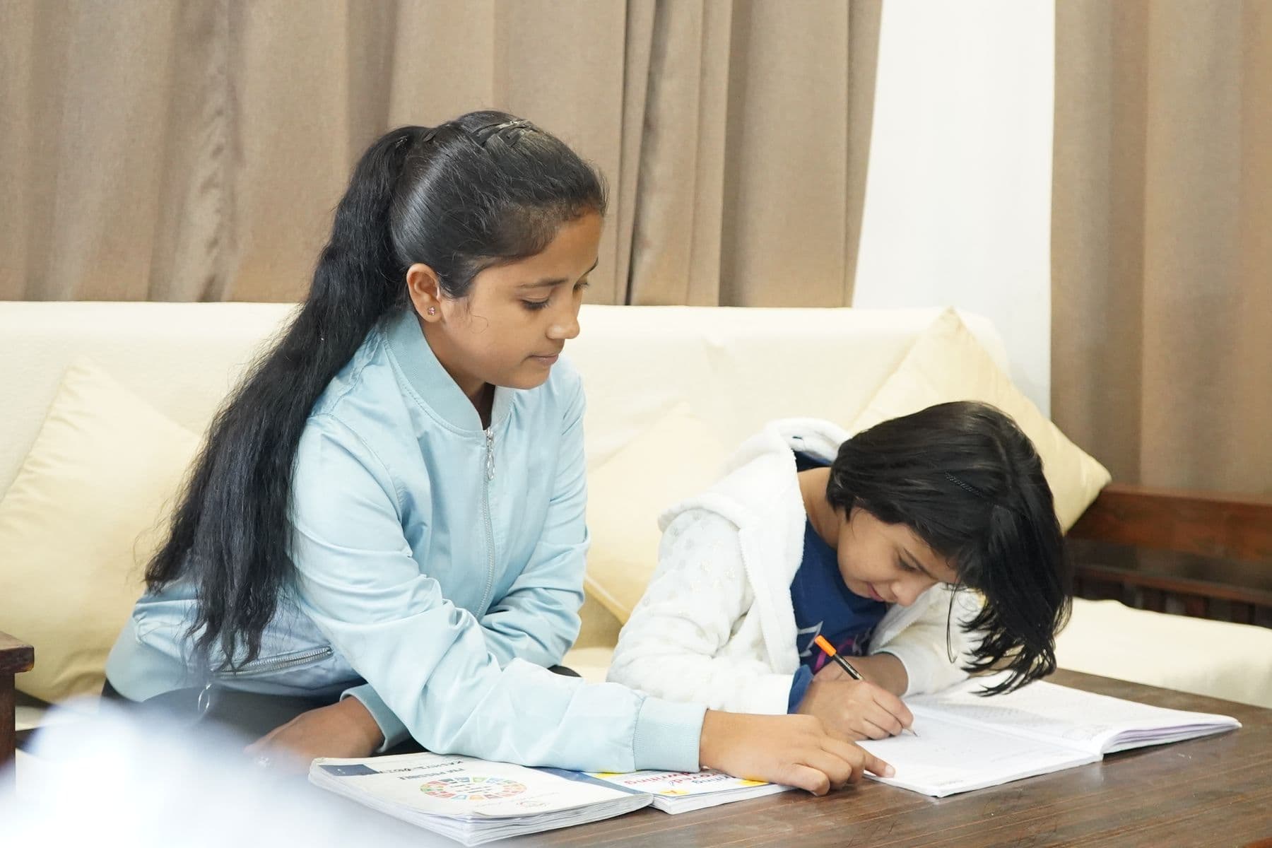 A home tutor helping a young student with her writing at home